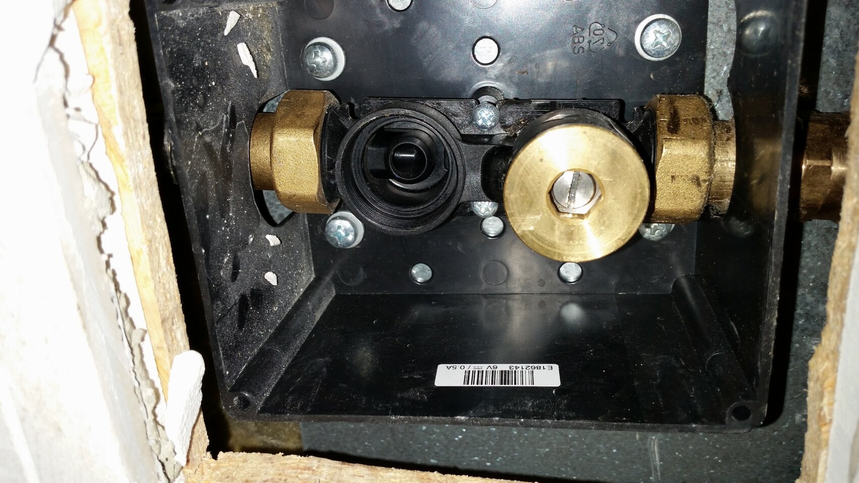 Close-up of valve and pipe system behind a wall with brass parts.