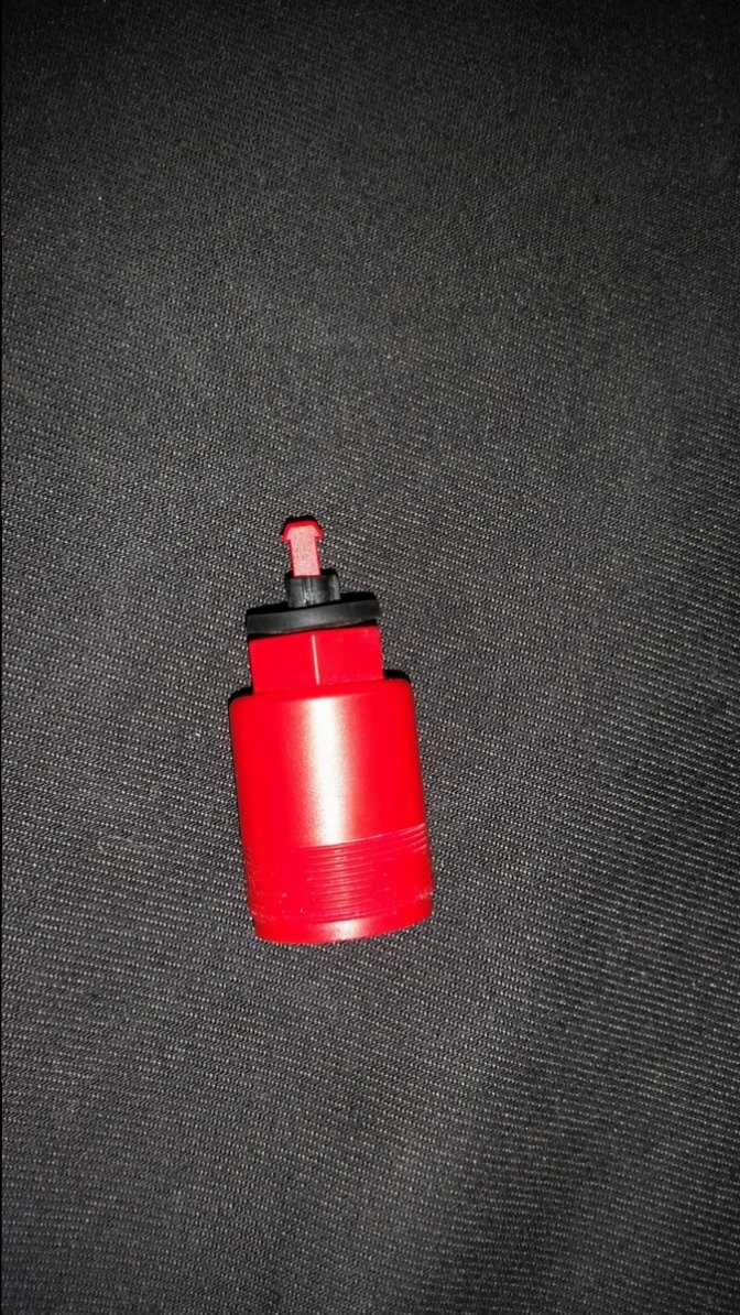 Small red plastic part with black cap on dark fabric background