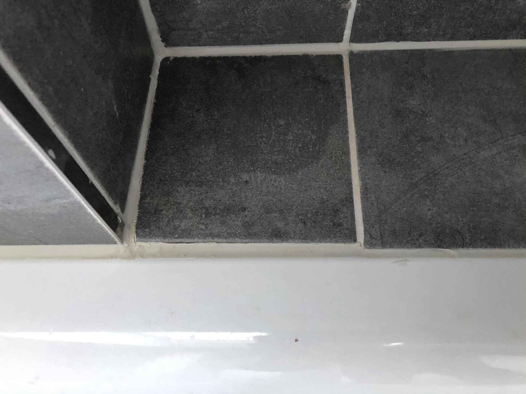Close-up of dark gray tiles with light grout lines, white edge at bottom.