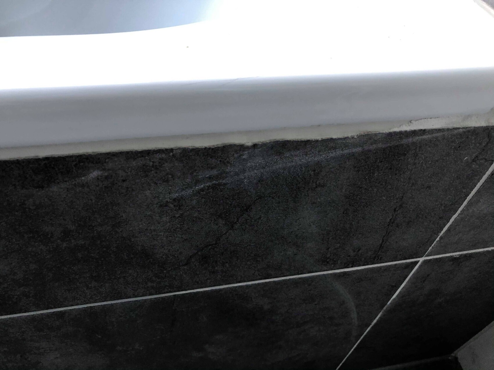 Close-up of black tiles with white grout lines and a white edge at the top of the image.