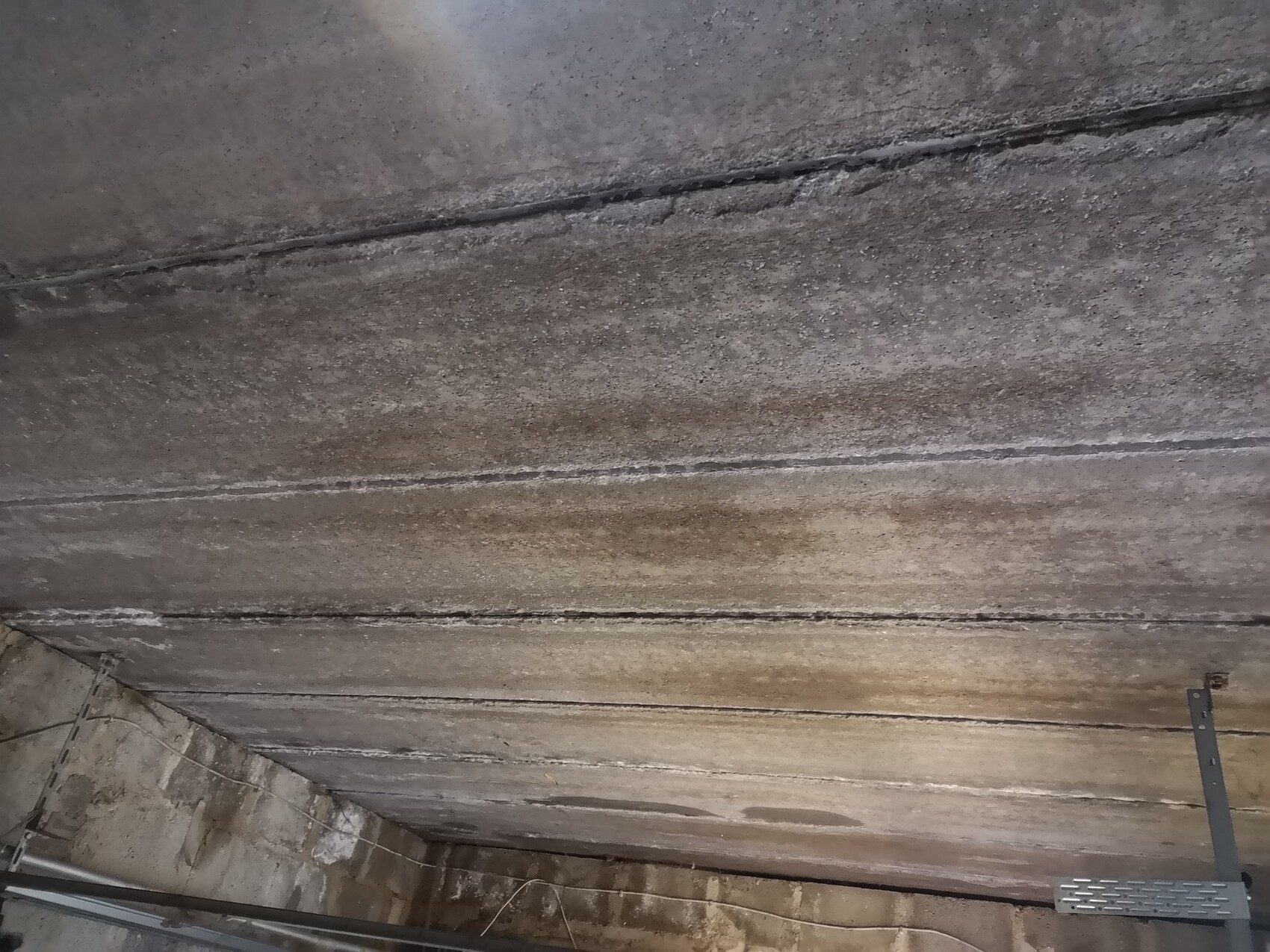 Basement concrete ceiling with moisture, darker streaks, and visible metal beams