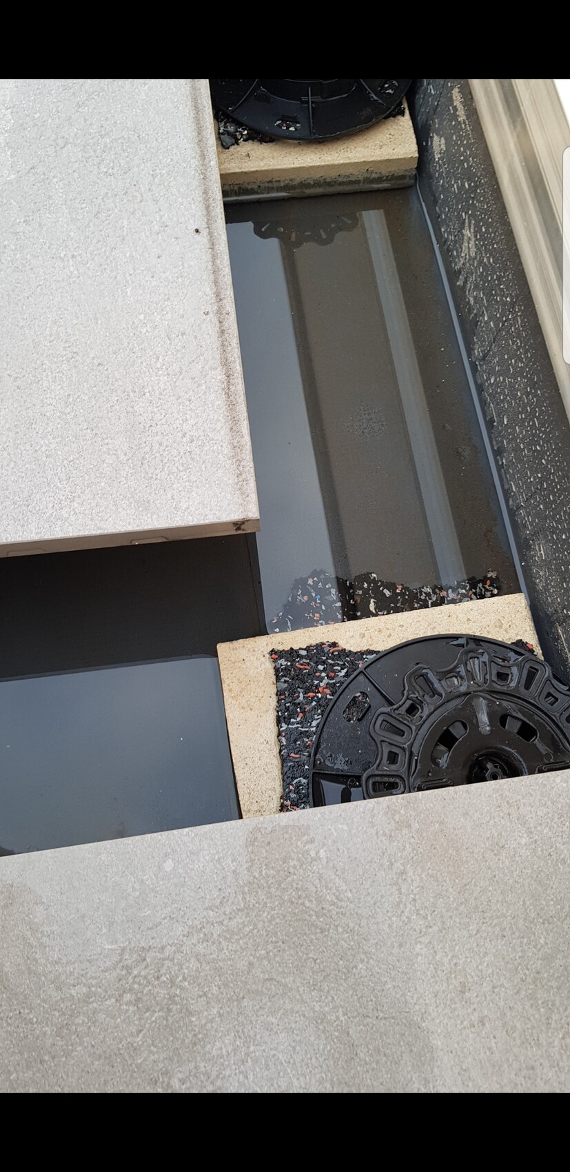 Wasserpfütze zwischen Steinplatten und rundem Kanaldeckel.