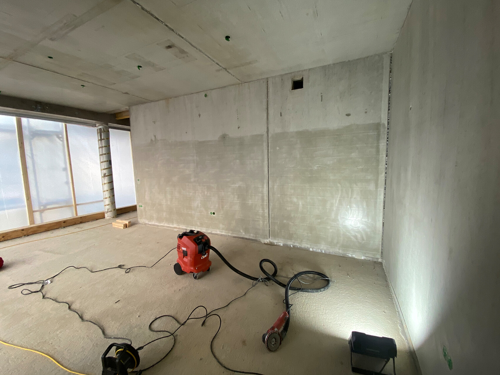 Baustellenraum mit Betonwänden, Kabeln auf dem Boden und rotem Staubsauger.
