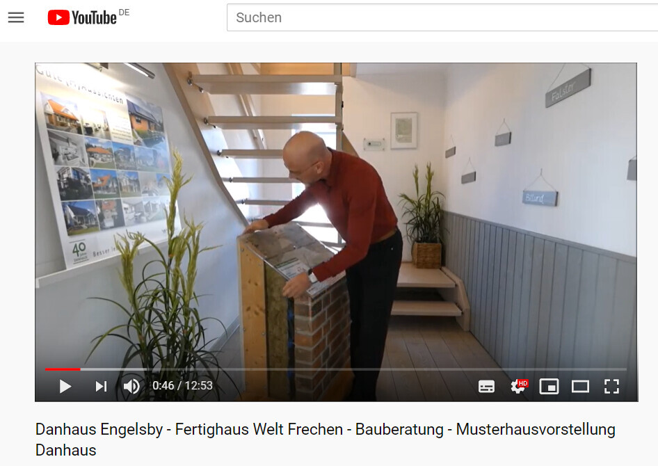 Man in red sweater inspecting a brick display in the model home showroom next to a staircase.