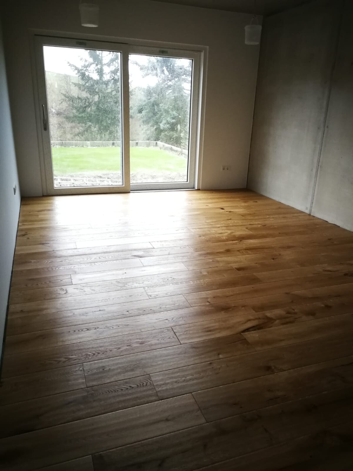 Empty room with wooden floor and large glass sliding door to the garden.
