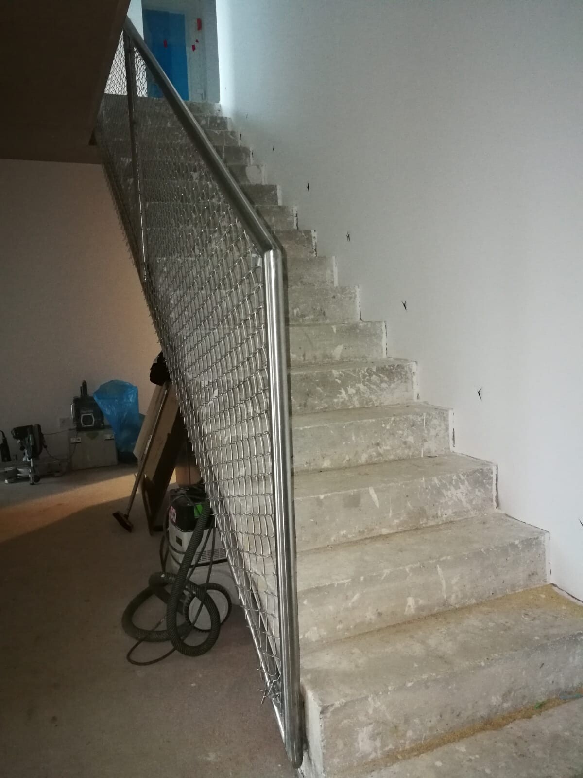 Concrete staircase with metal mesh railing in a construction project; tools bottom left.