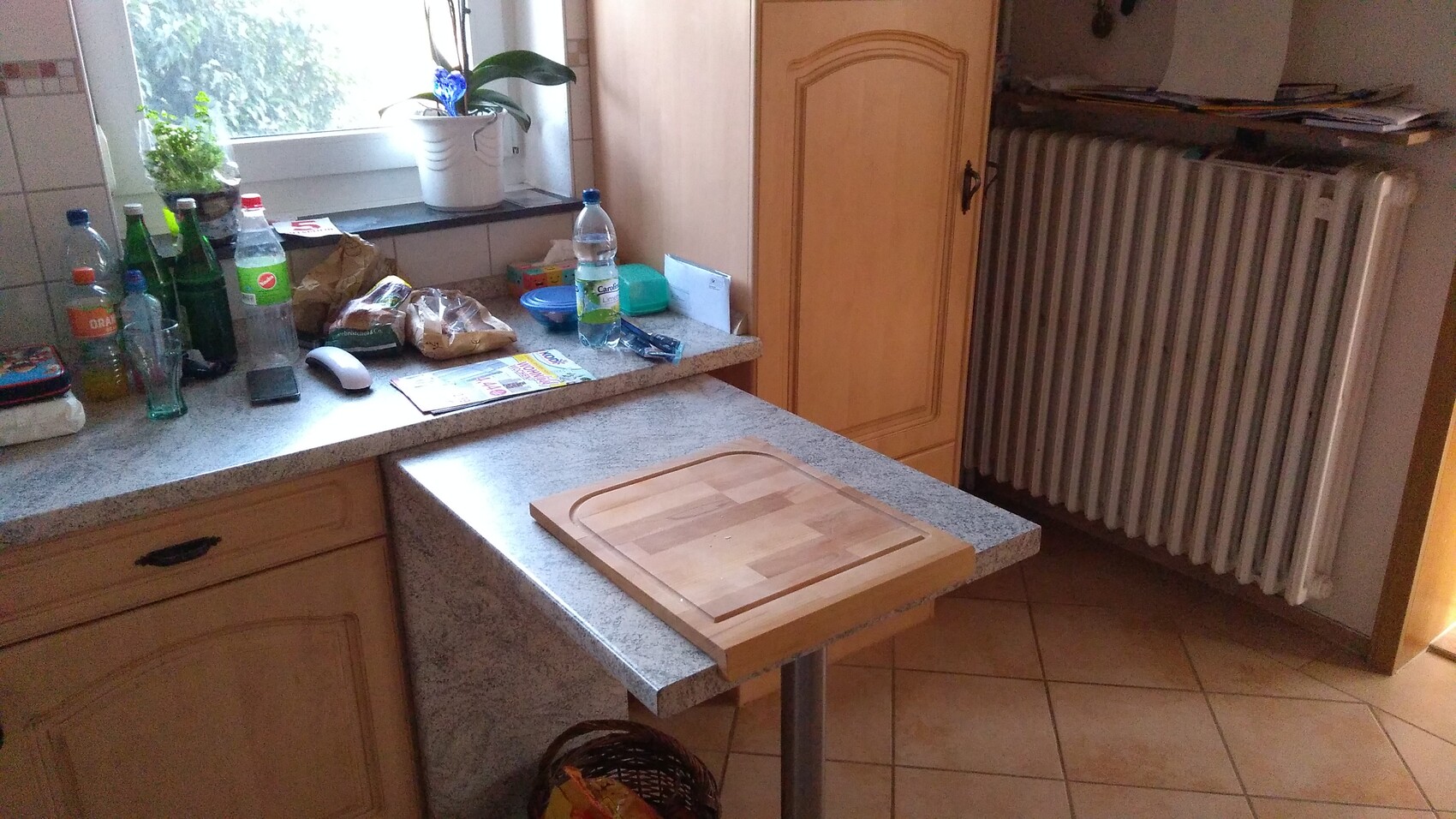 Küche mit Chaos auf der Arbeitsplatte: Flaschen, Snacks, Brot, Schneidebrett auf dem Tisch.