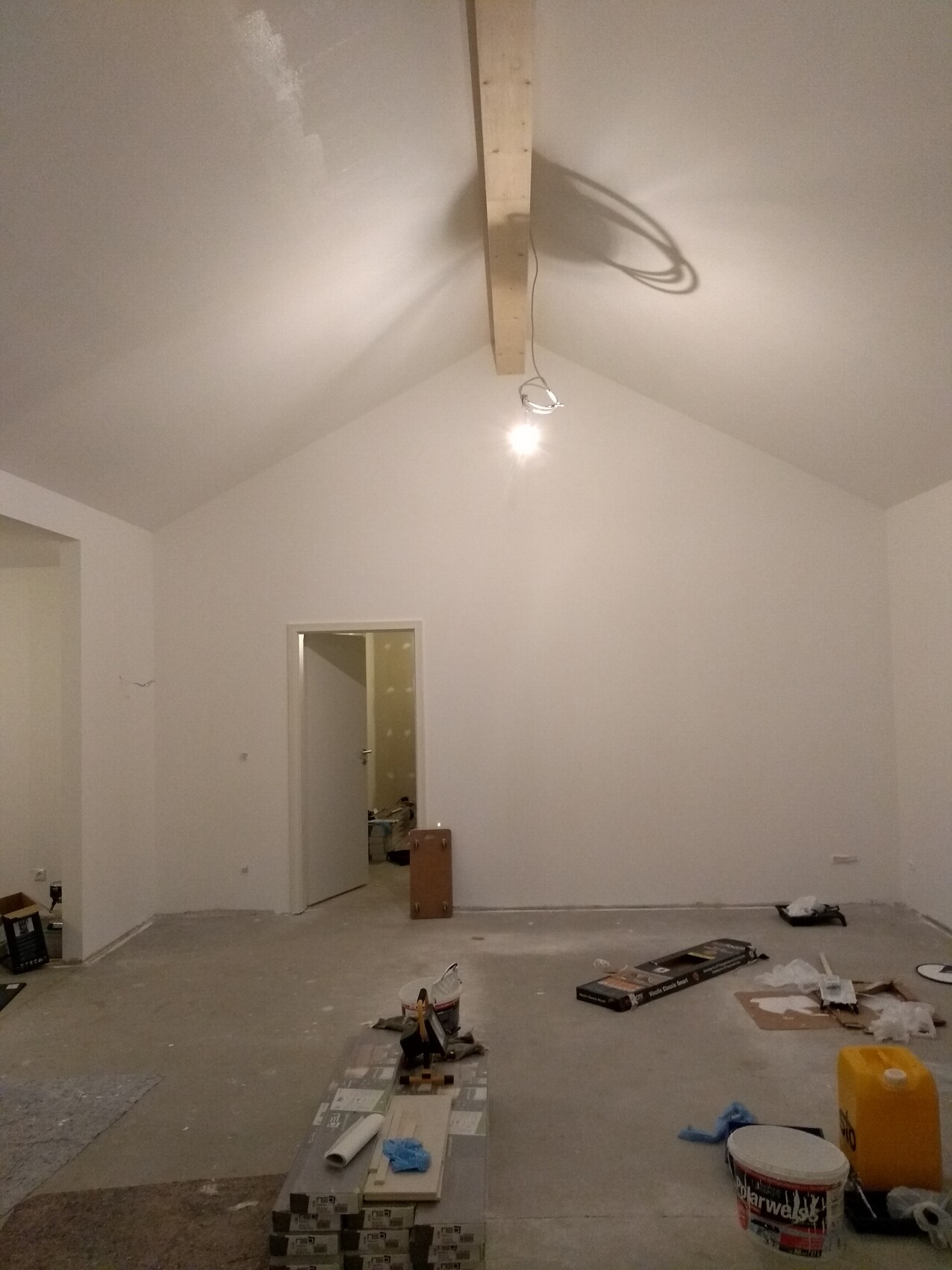 Unfinished room with pitched roof, exposed wooden beam, open door, and building materials.