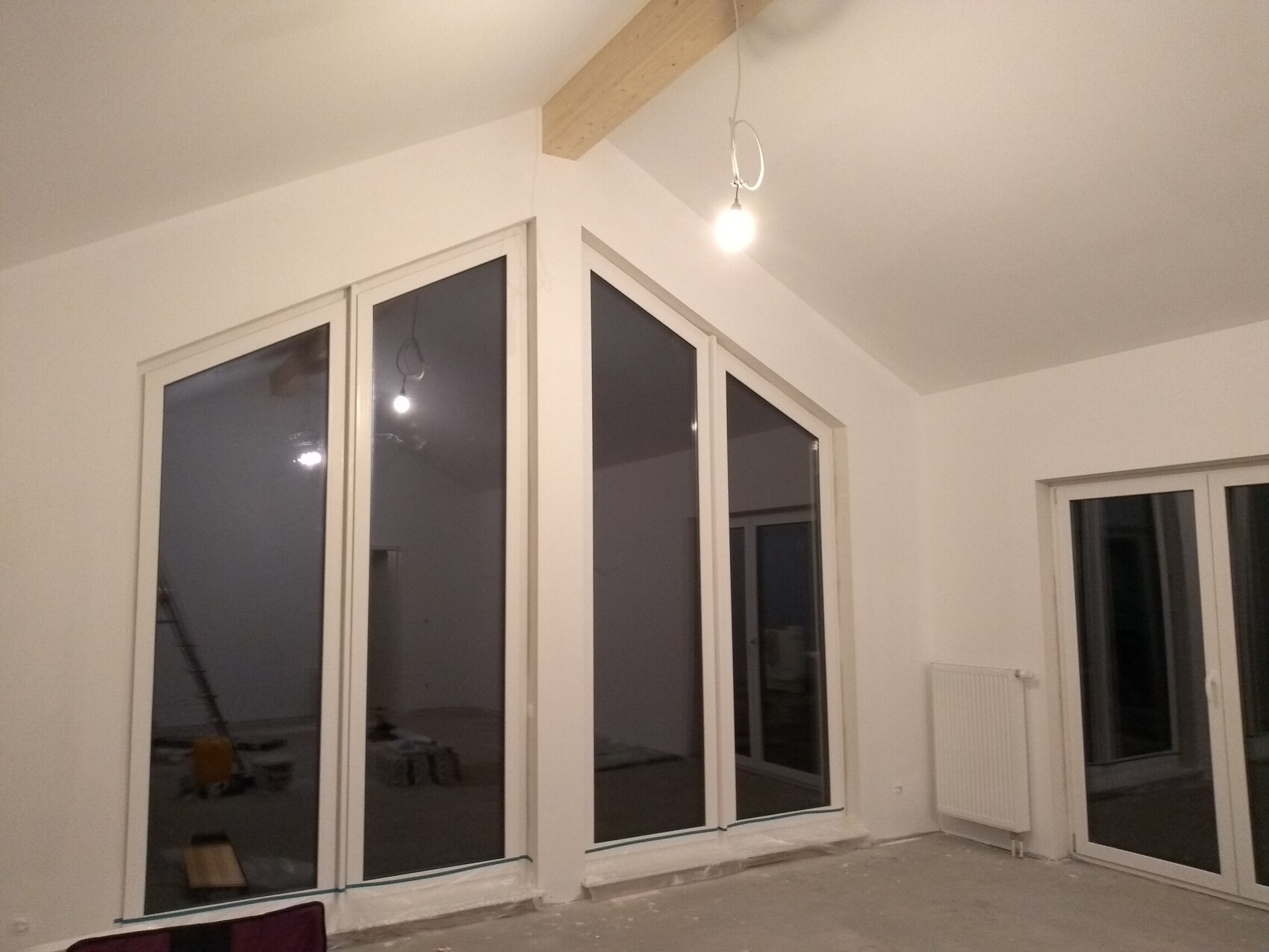 Interior with large corner glass facade, white walls, bare floor, hanging light bulb.