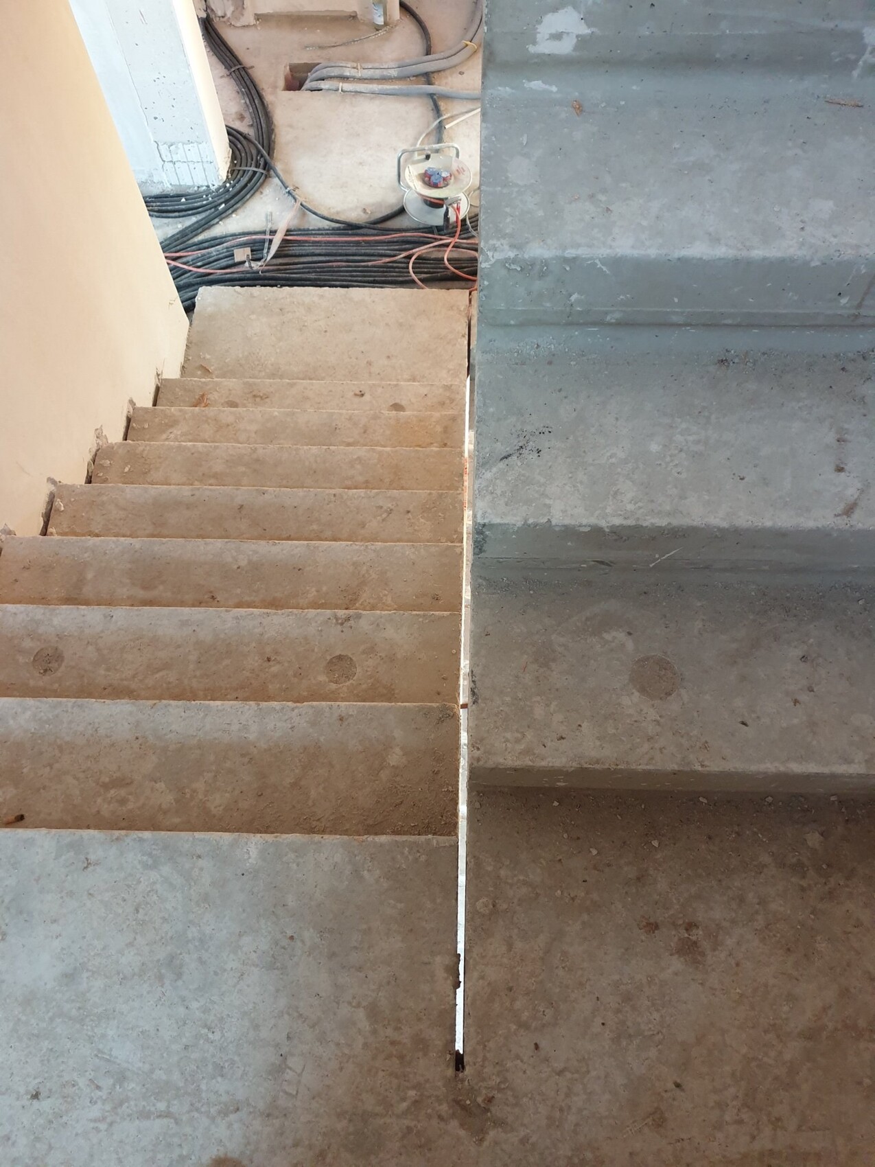 Unfertige Betonstufen auf einer Baustelle; im Hintergrund liegen Kabelstränge und Werkzeuge.