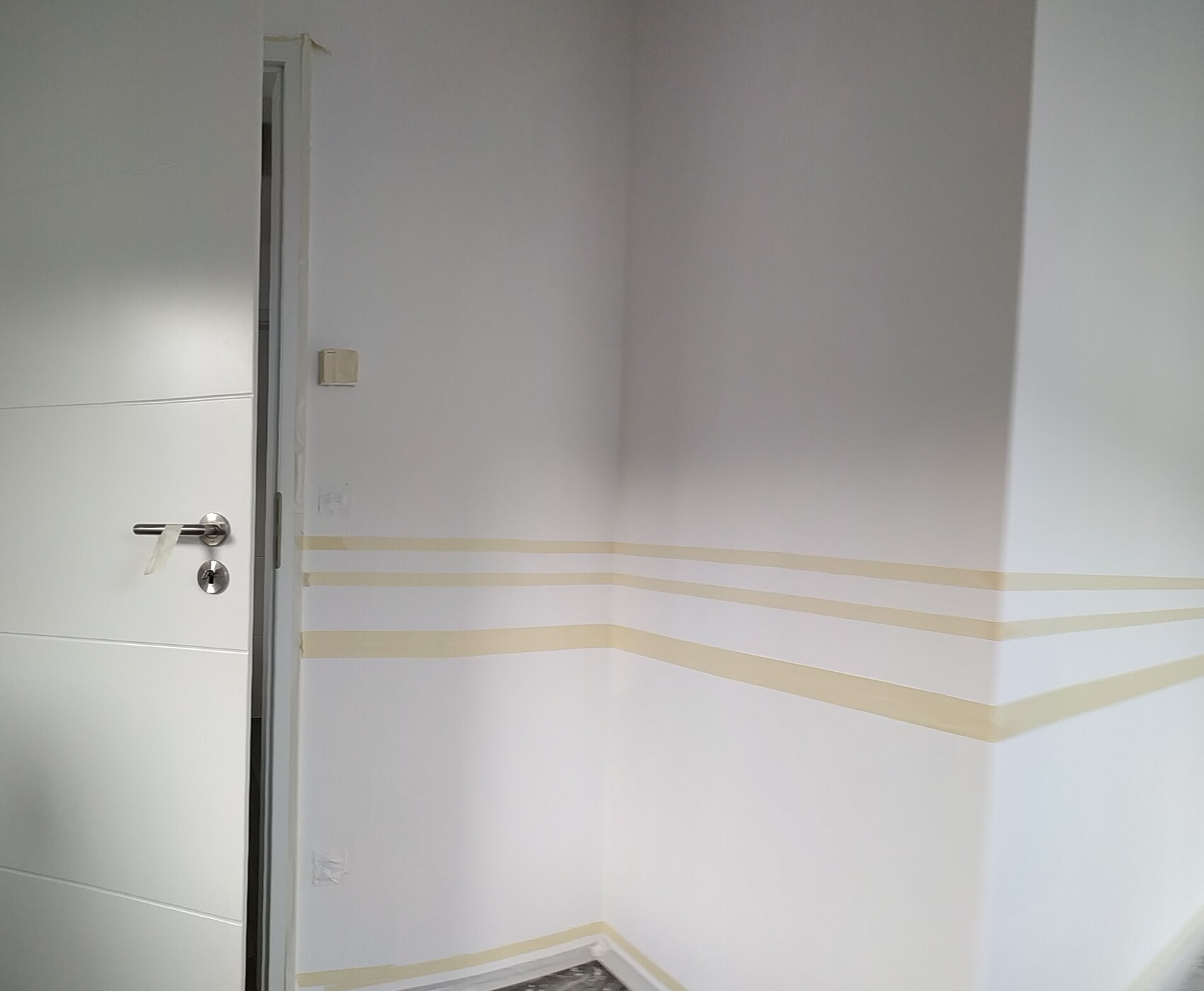 White interior wall with door, walls masked for painting, painter’s tape lines visible