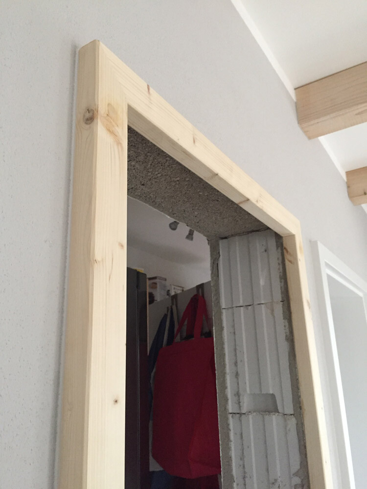 Türöffnung mit neuem Holzrahmen in grauer Wand; Innenraum mit Kleiderhaken sichtbar.
