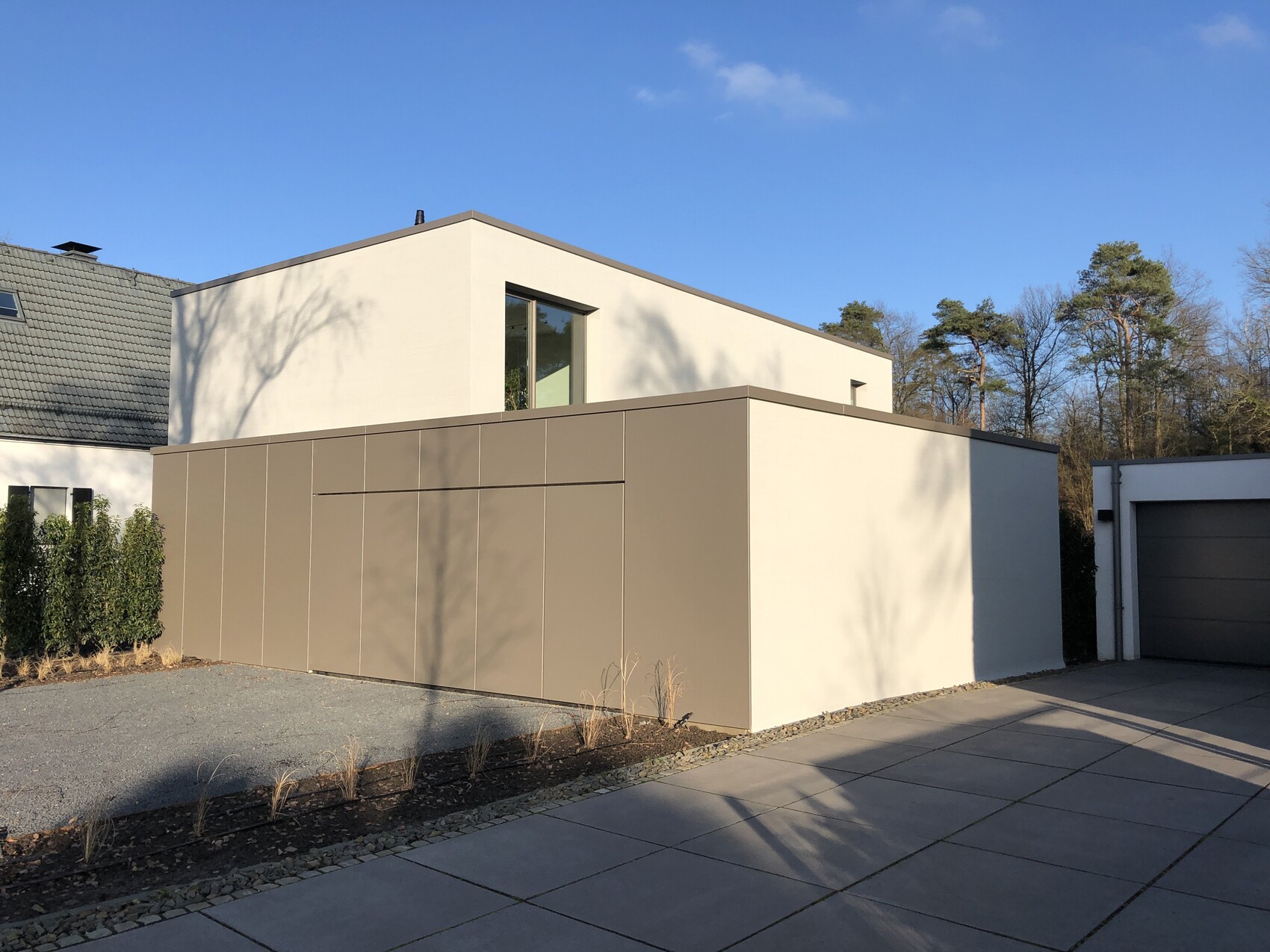 Modern house facade with flat roof, beige exterior, garage, and driveway.