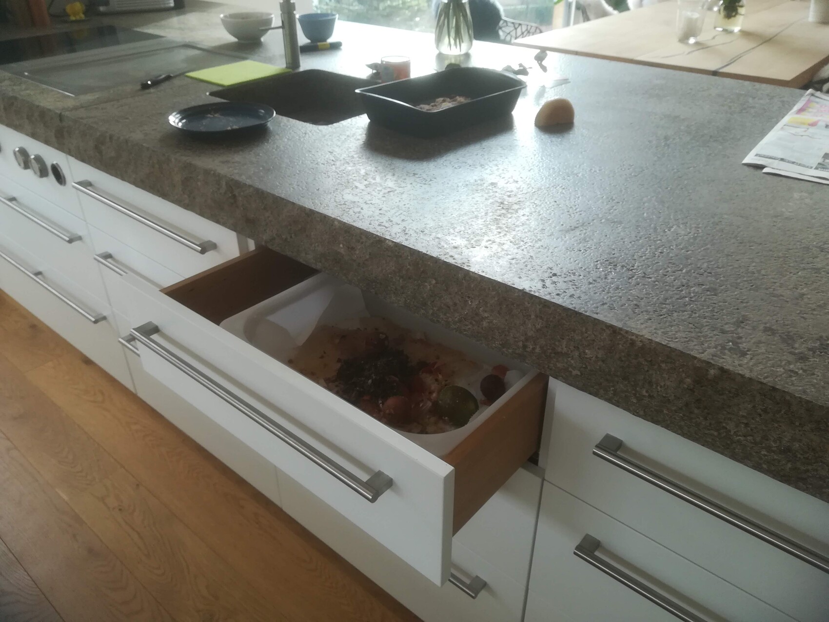 Modern kitchen island with gray granite countertop; open drawer showing food/container, plates next to it.