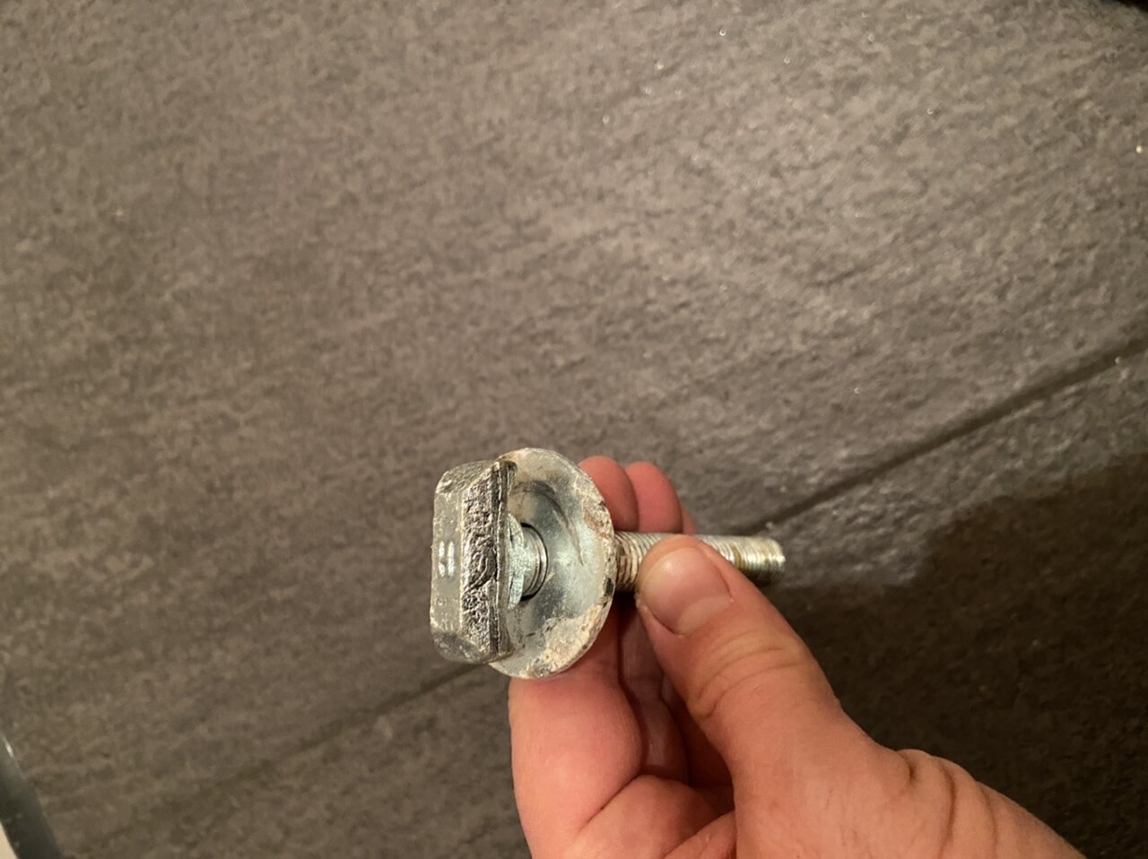 Close-up of a metal bolt with thread and round head, held in a hand.