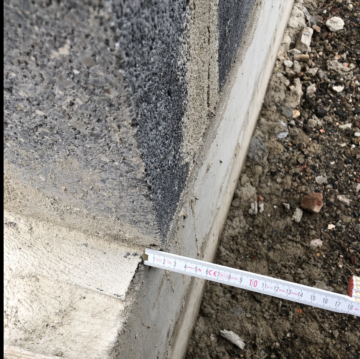 Concrete foundation with dark moisture on the wall; measuring tape on the floor.