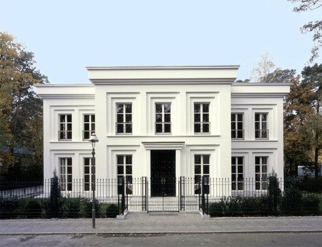 White, two-story villa with symmetrical facade, central entrance, and garden fences in front of the street.