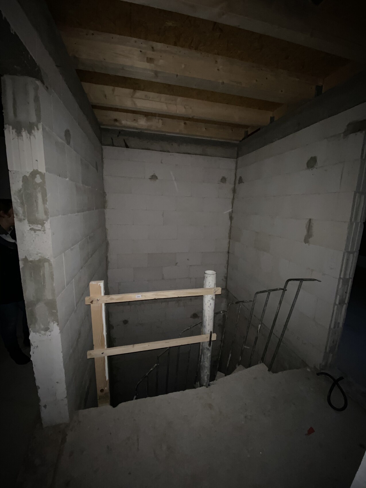 Stufenabgang in unfertigem Kellergeschoss mit provisorischer Holzbarrikade und Metallgeländer.