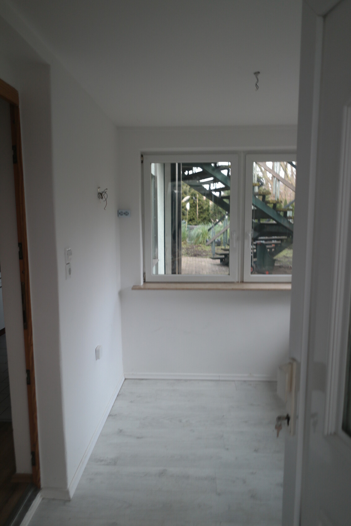 Bright, empty interior with window to outdoor stairs; exposed cables on the wall.