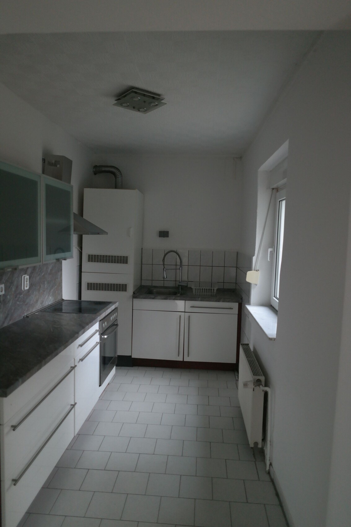 Small modern kitchen with sink, stove, extractor hood, white cabinets, and window.