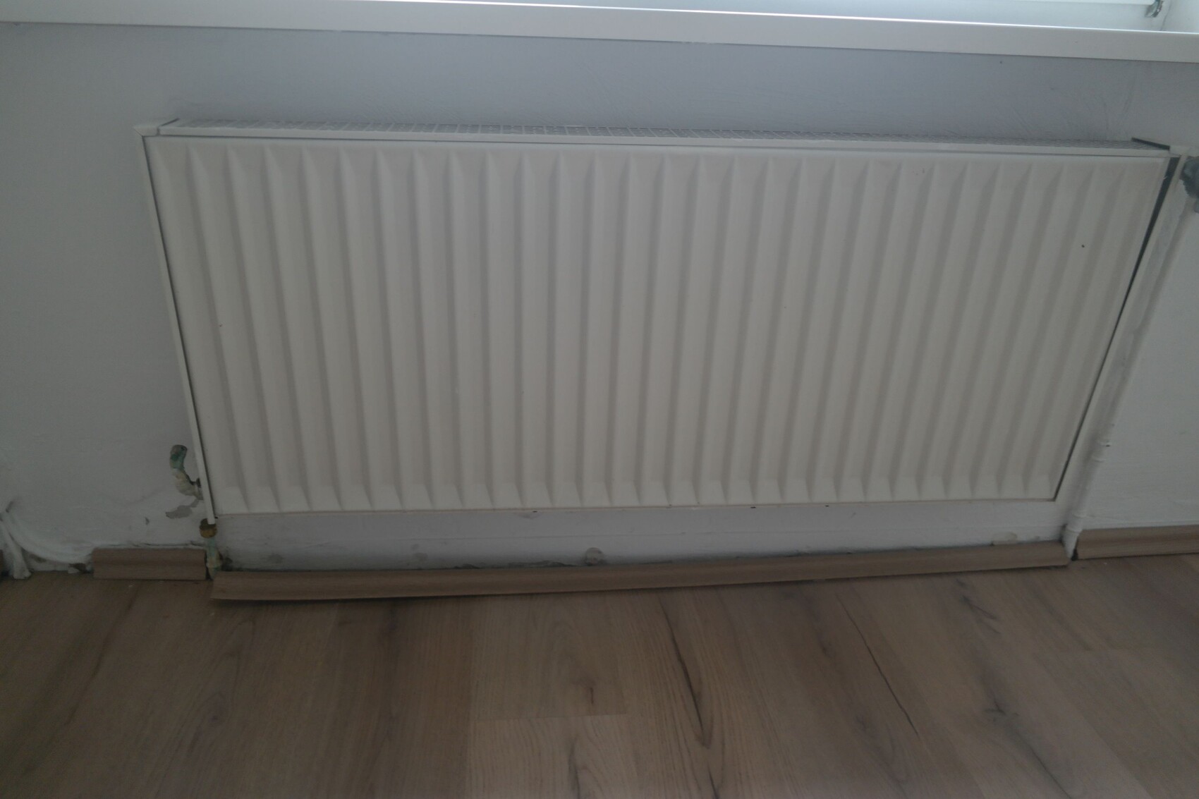 White radiator with vertical panels on wall above wooden floor.