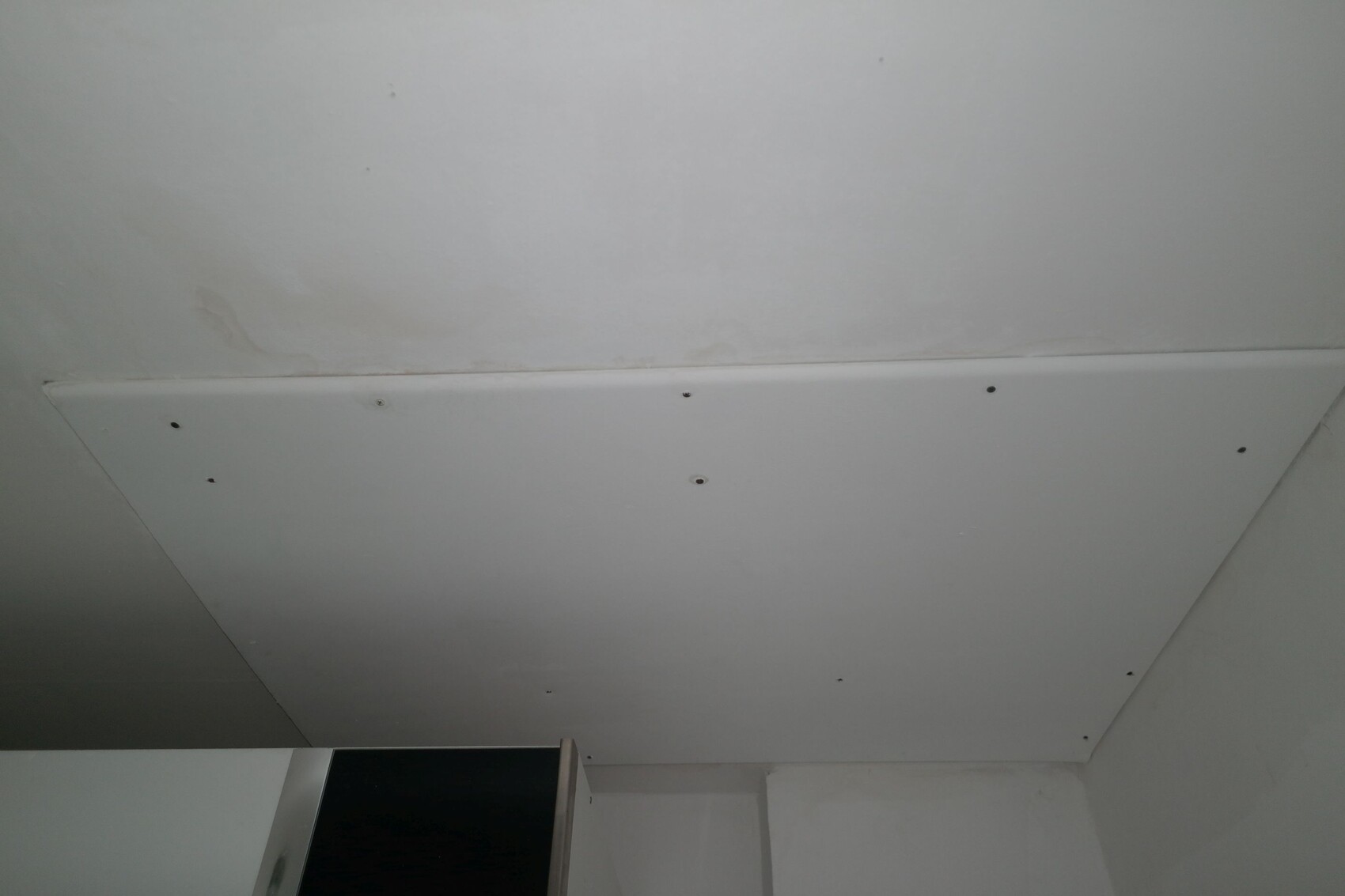 White drywall ceiling panel with visible screw heads, view toward room corner.