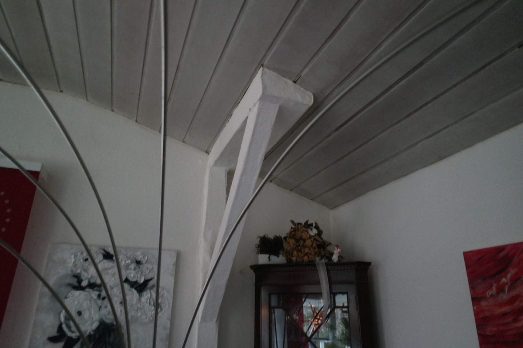Interior corner: white diagonal support, gray ceiling panels, dark display cabinet with decoration.