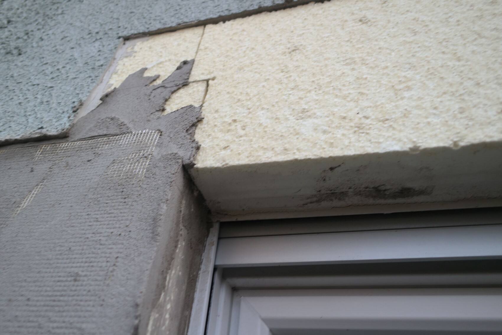 Close-up of a facade with peeling plaster above the window frame.