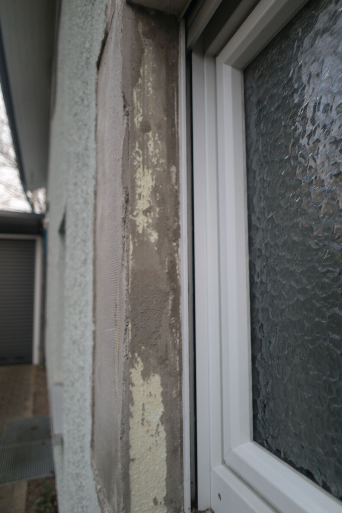 Close-up of a window frame next to a wall with peeling paint and textured glass.