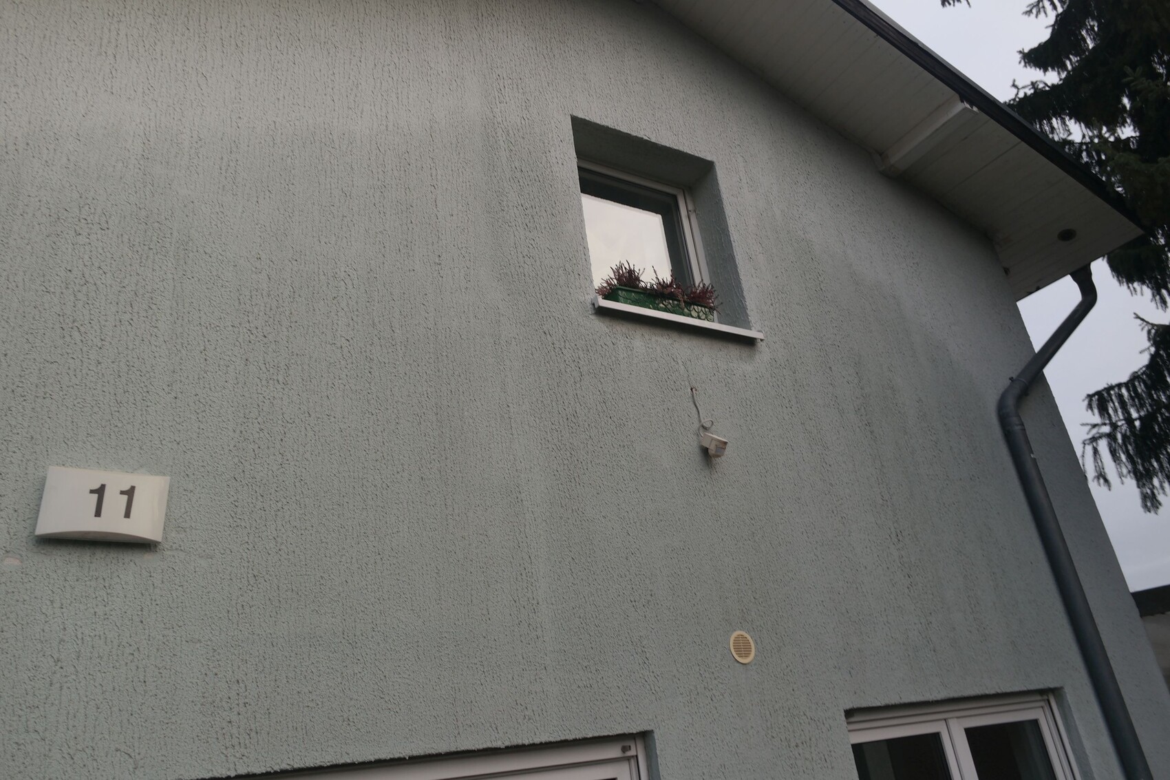 Exterior wall of a house with small window and flower box, house number 11, rainwater downpipe on the right.