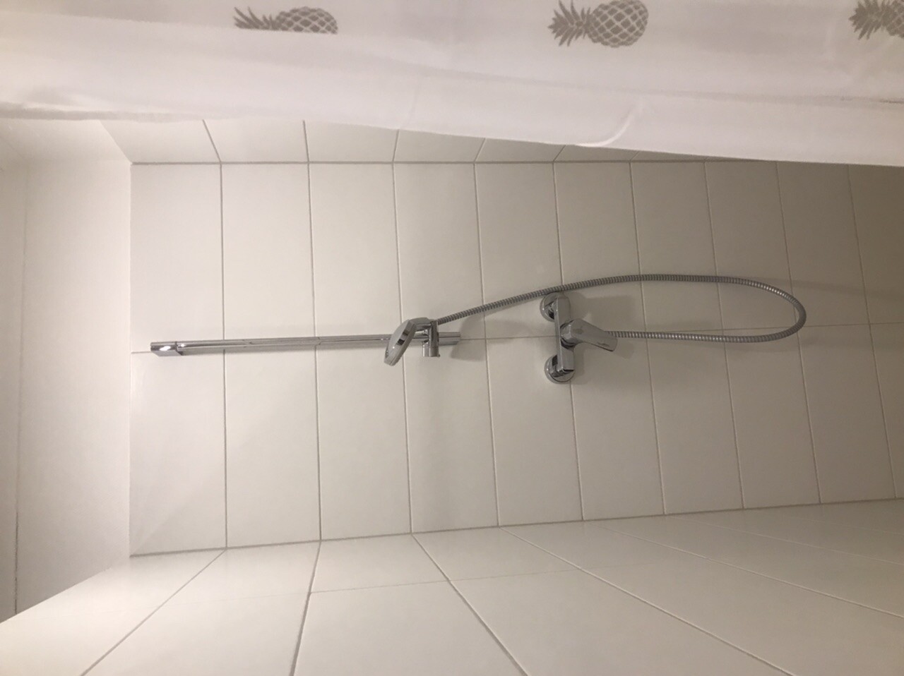 Hand shower on wall mount in front of white bathroom tiles in a bathroom.