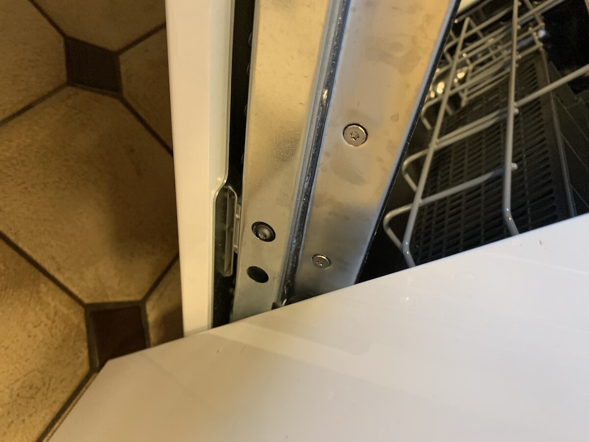 Opened dishwasher from the side; interior basket, metal frame and screws visible.