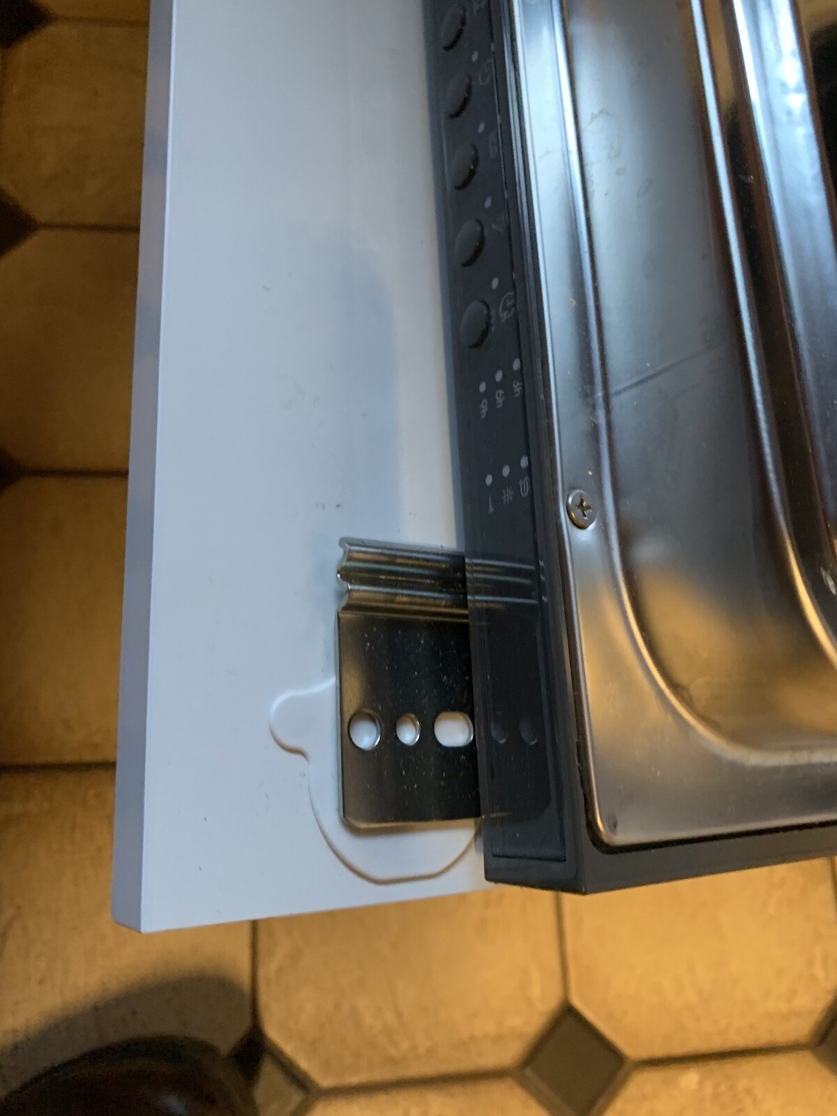 Close-up of a kitchen appliance with metal frame, screw and black panel.