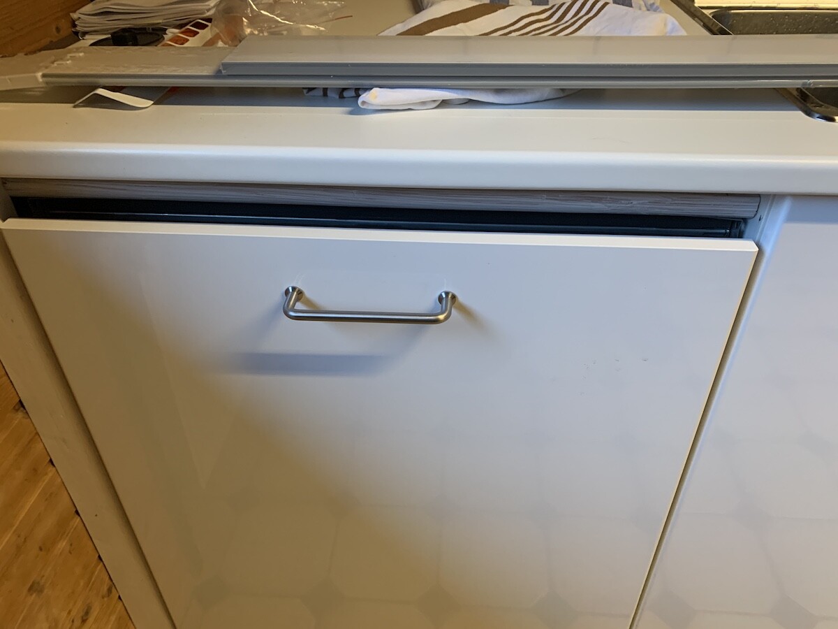 White dishwasher in the kitchen with metal handle; fabrics placed on top.