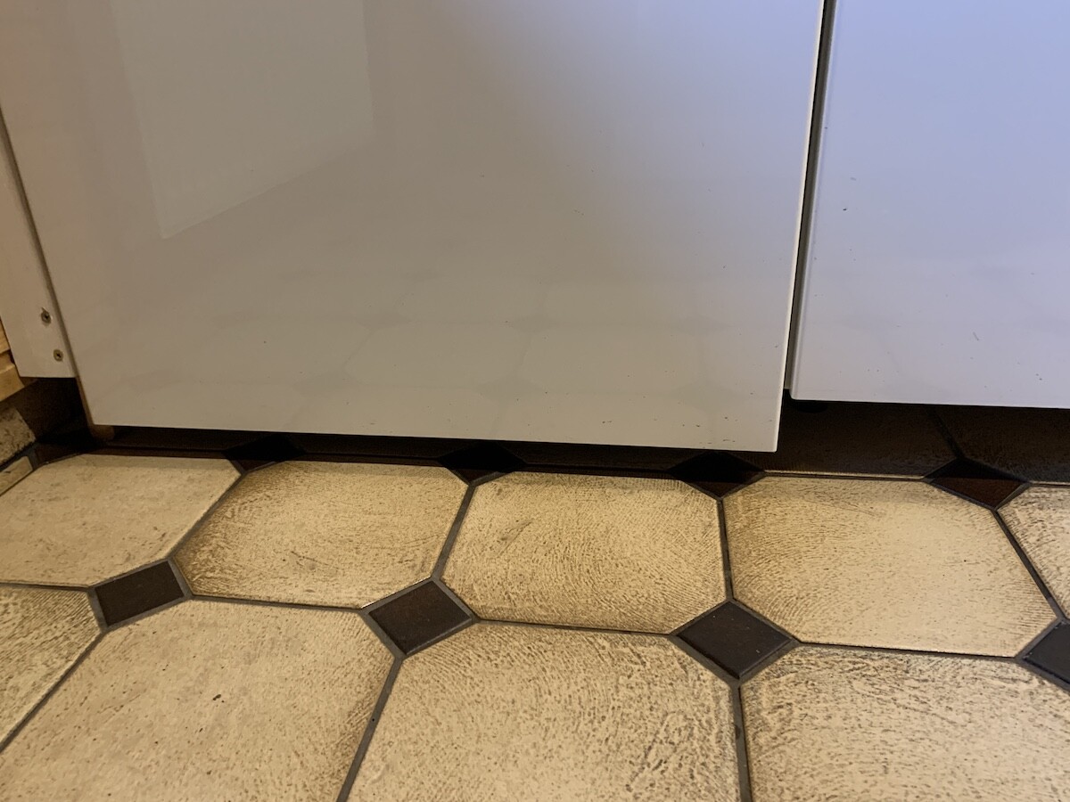 Underside of a white kitchen appliance in front of floor tiles in the kitchen.