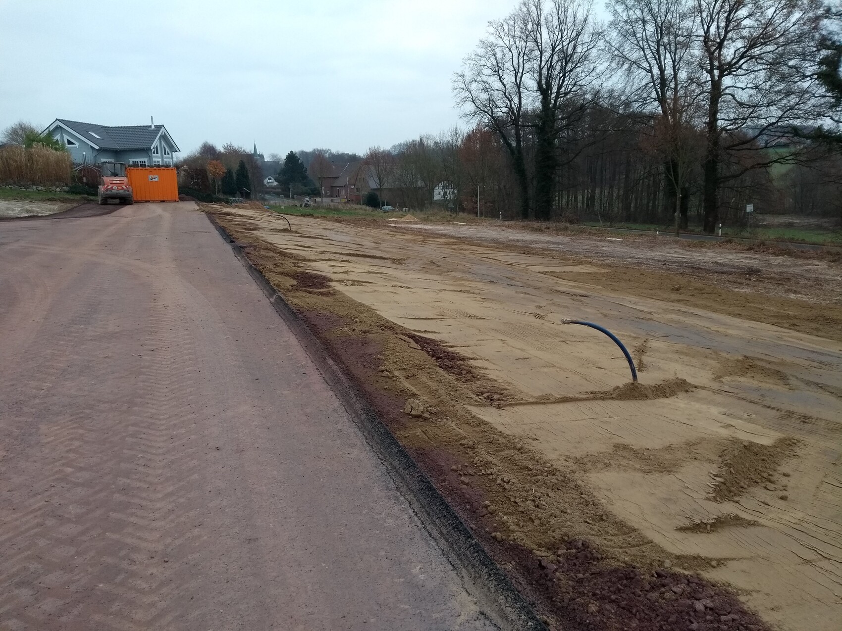 Construction site on a residential street: sandy soil, blue pipe, orange construction container in the background.
