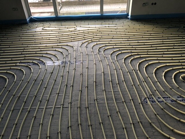 Underfloor heating pipes arranged in loops across the floor of an empty room.