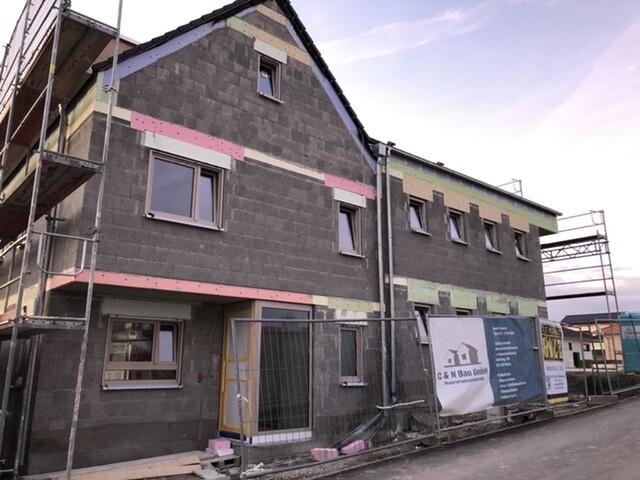 Multi-story shell construction with windows, scaffolding, and construction fence on a building site.