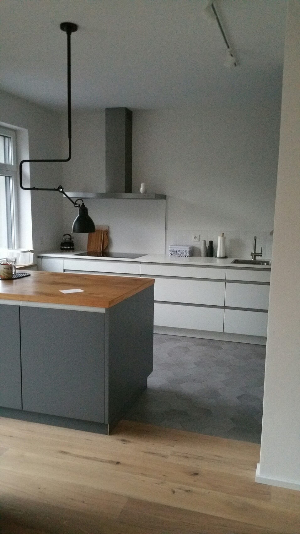 Modern kitchen with gray base cabinets, wooden island, black industrial lamp, sink.