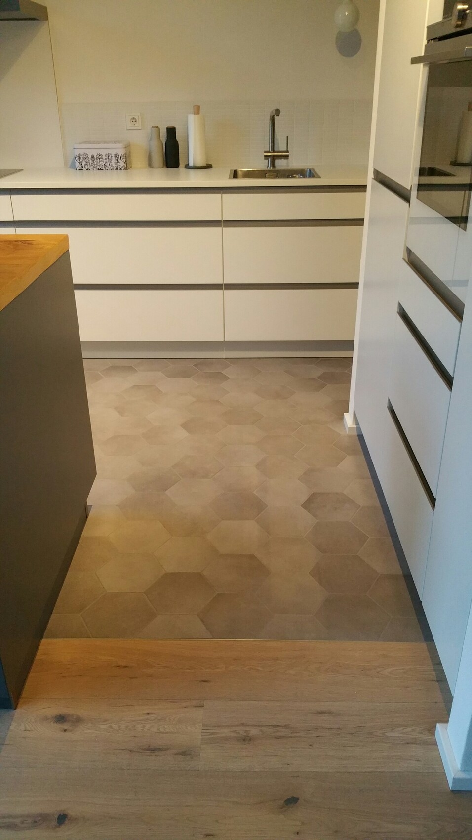 Modern kitchen with white cabinets, sink, faucet, and gray hexagonal floor tiles.