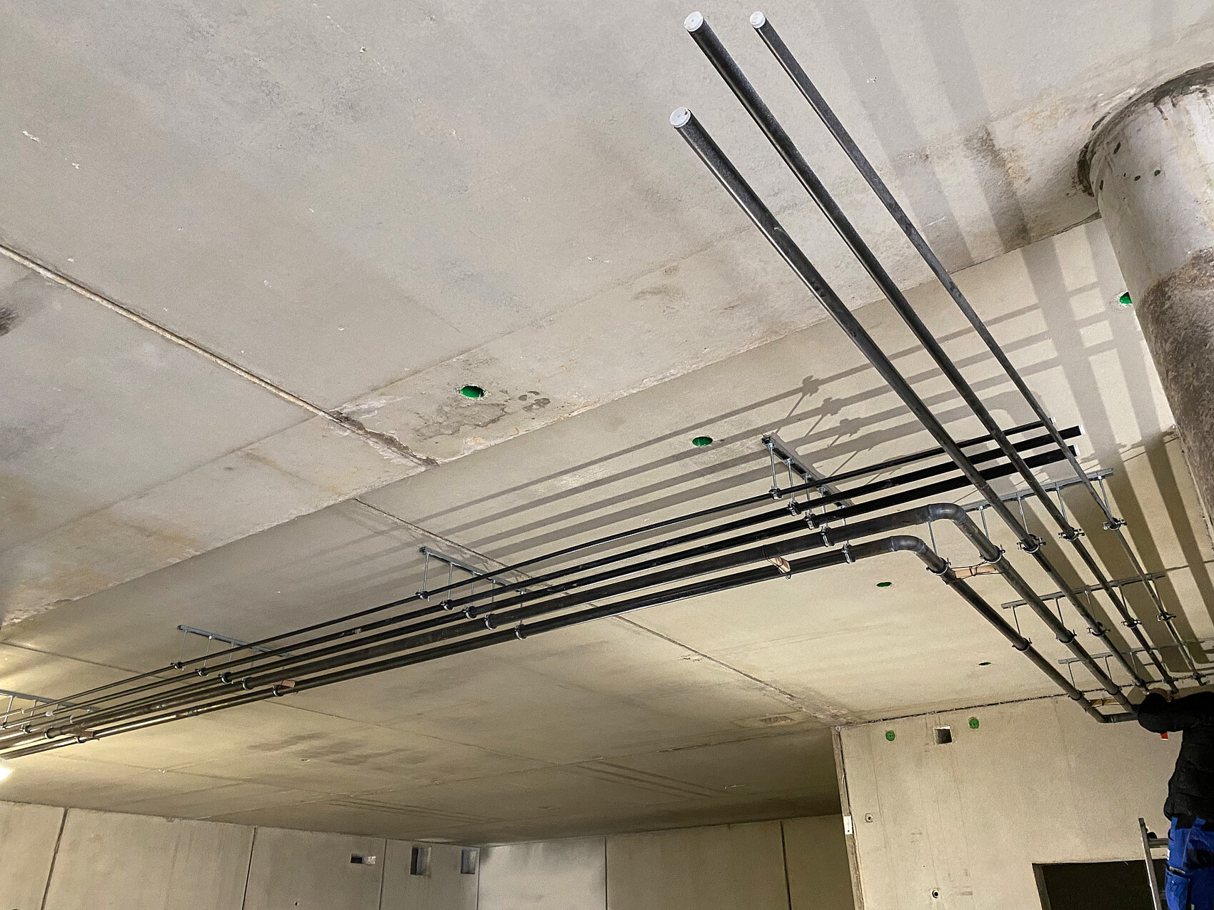 Black pipes running parallel under the ceiling, with brackets and green markings.