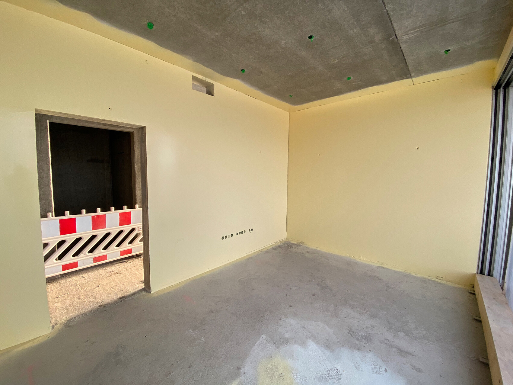 Unfinished interior with yellow walls, raw concrete floor, and door to the construction site with barrier tape.