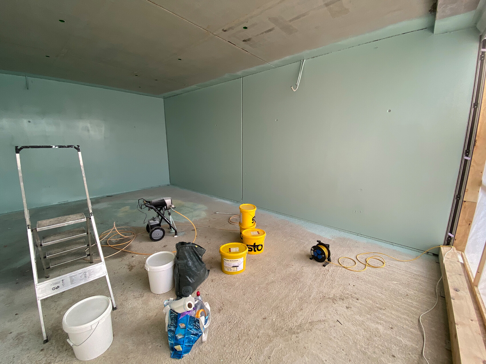 Unfinished room with green drywall, ladder on the left, yellow buckets and extension cord.