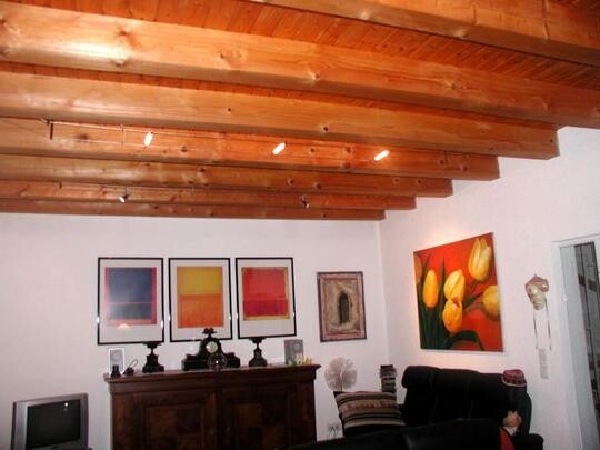 Living room with wooden beam ceiling, dark sofa, and colorful wall pictures.