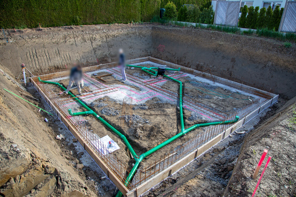 Excavated construction site with foundation, reinforcement, and green pipes during installation