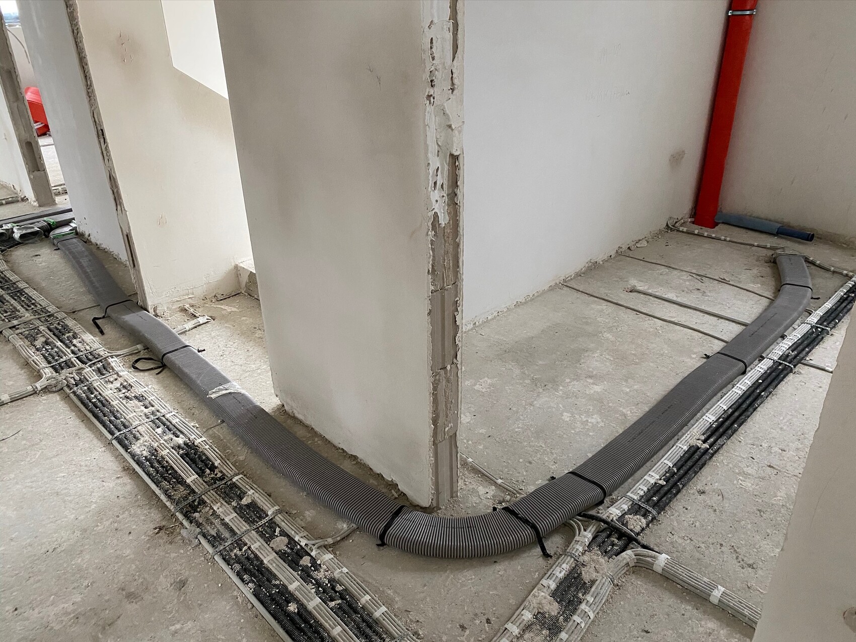 Construction site: cable ducts and flexible pipes run along the floor, red pipe on the wall.