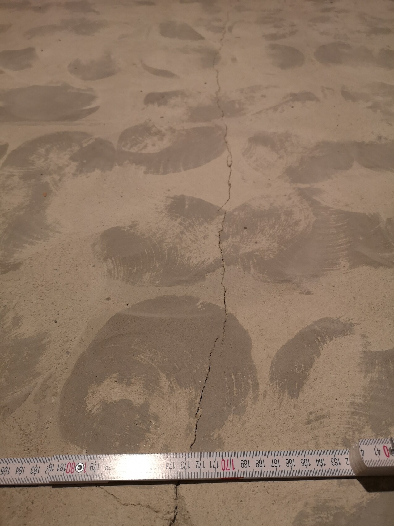 Concrete floor with many round handprints in the dust, a central crack line runs through, measuring tape on the floor.