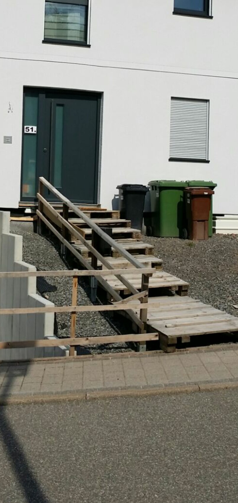 White house with dark door, wooden pallet stairs and trash bins in front of entrance 51