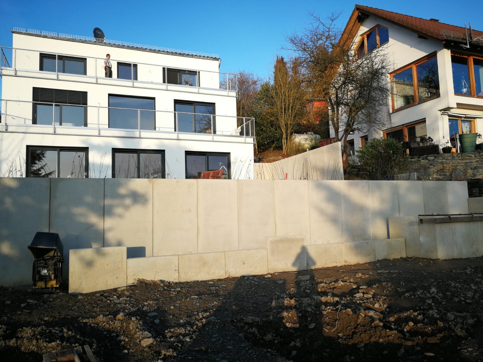Moderne weiße Gebäude mit Balkonen hinter Betonmauern; Baugelände im Vordergrund.