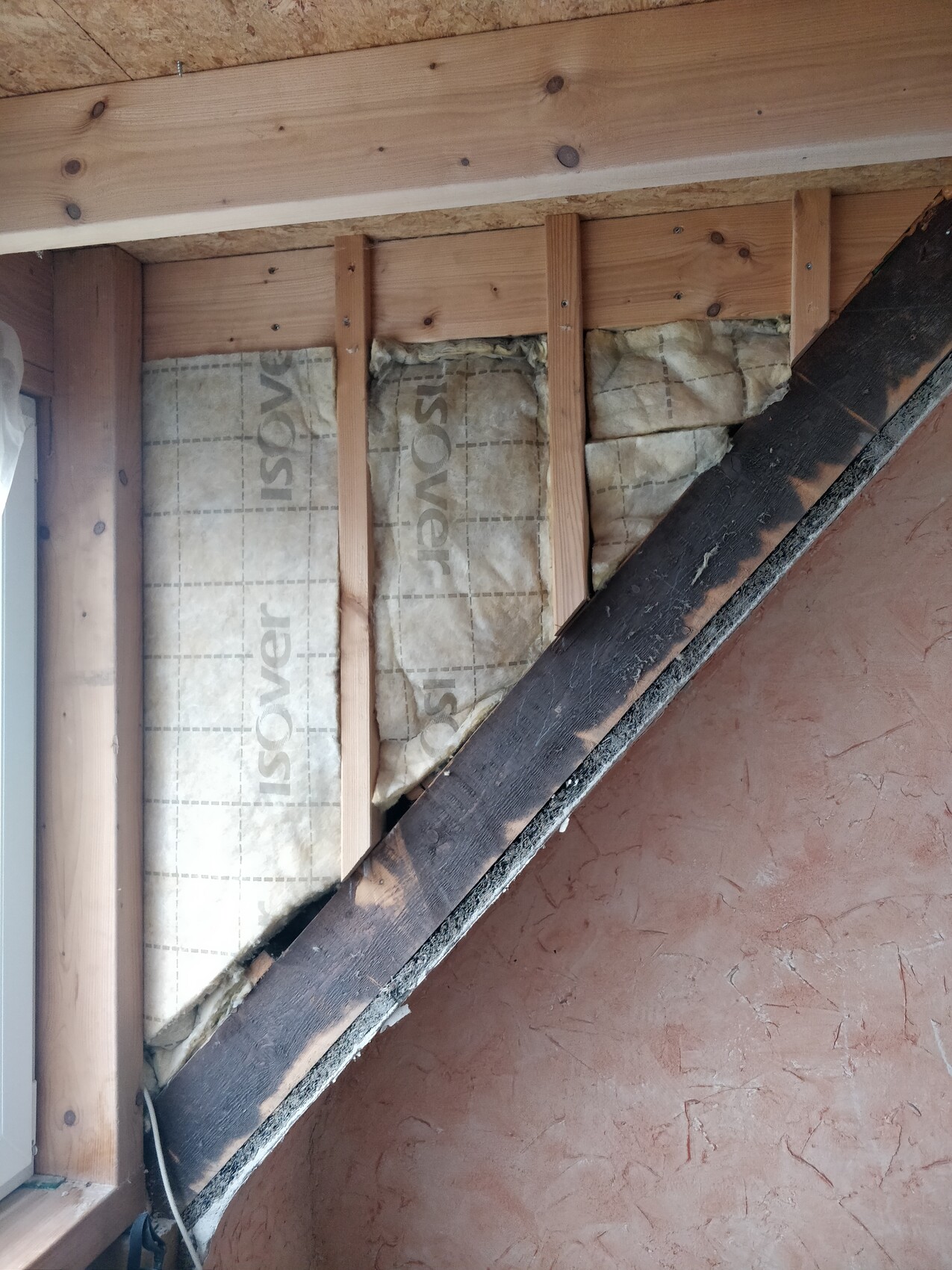Attic wall with wooden studs and Isover insulation, diagonal wooden beam visible